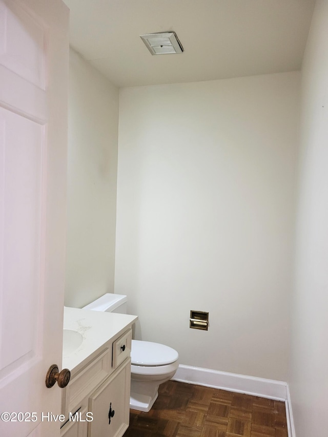 half bath with vanity, toilet, visible vents, and baseboards