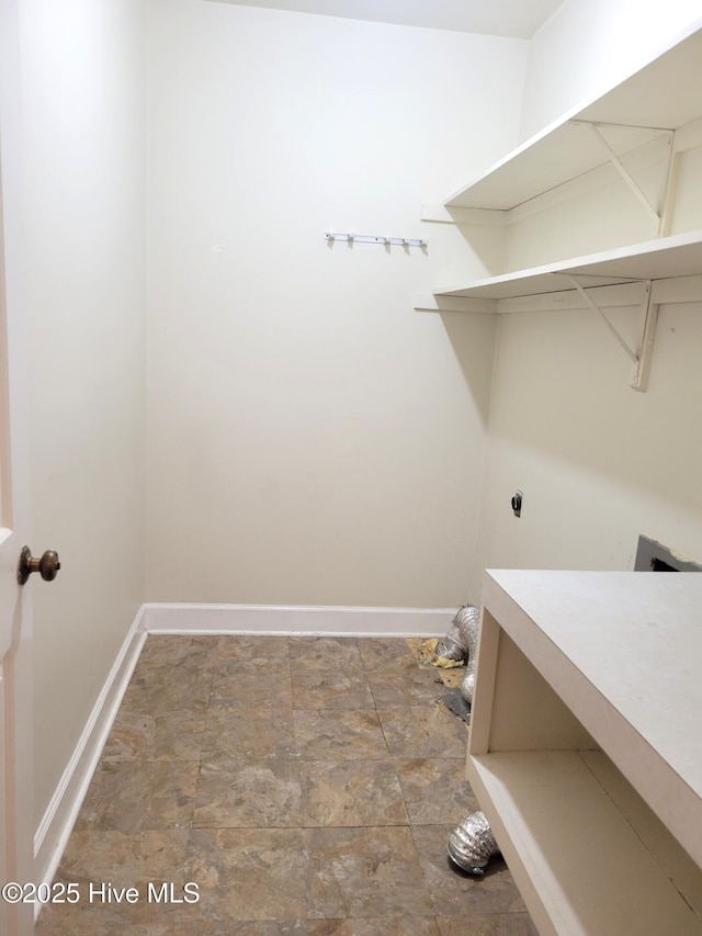 laundry area featuring laundry area, baseboards, hookup for an electric dryer, and stone finish flooring