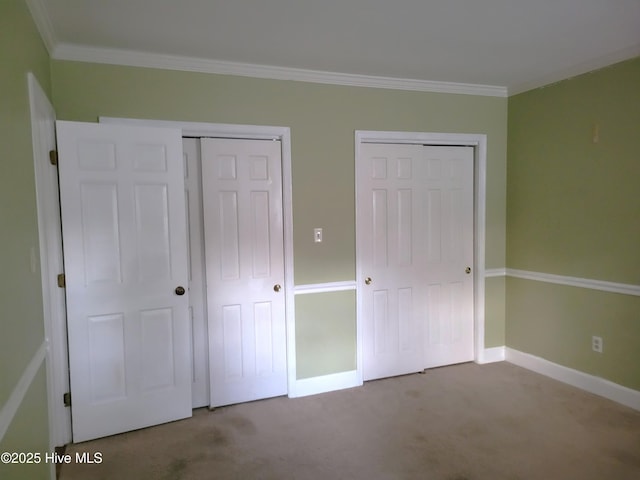 unfurnished bedroom featuring baseboards, multiple closets, carpet floors, and ornamental molding