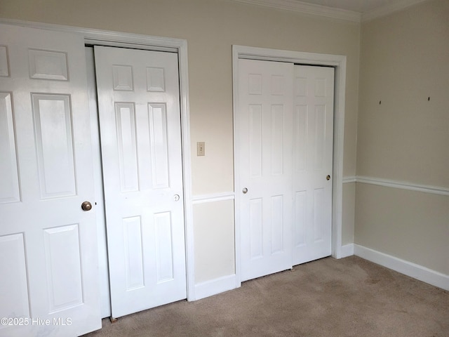 unfurnished bedroom with baseboards, carpet floors, multiple closets, and crown molding