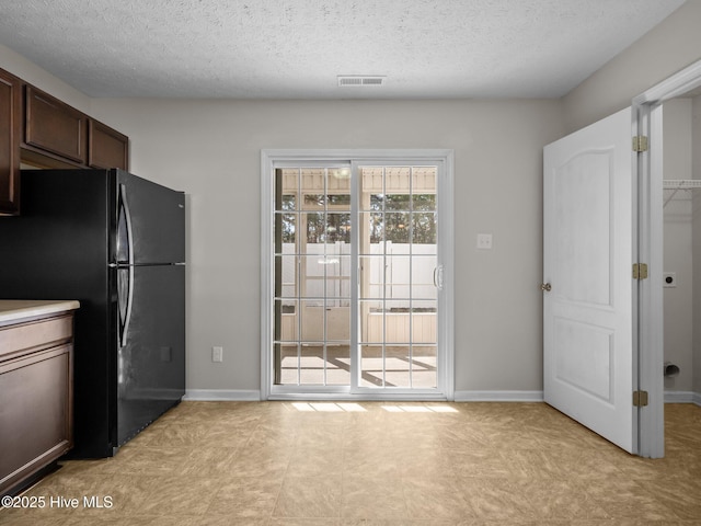 kitchen featuring a textured ceiling, black fridge, and dark brown cabinets