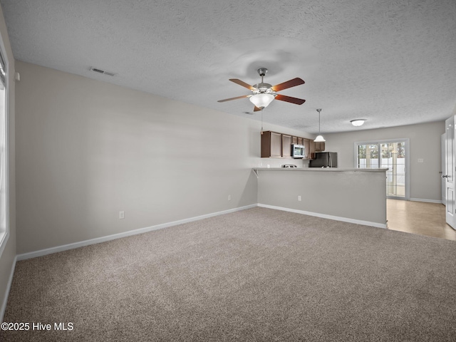 unfurnished living room featuring light colored carpet, ceiling fan, and a textured ceiling