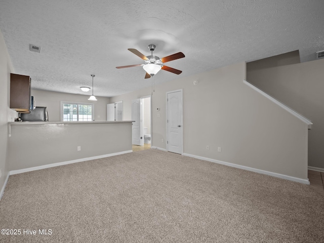 unfurnished living room with light carpet, ceiling fan, and a textured ceiling