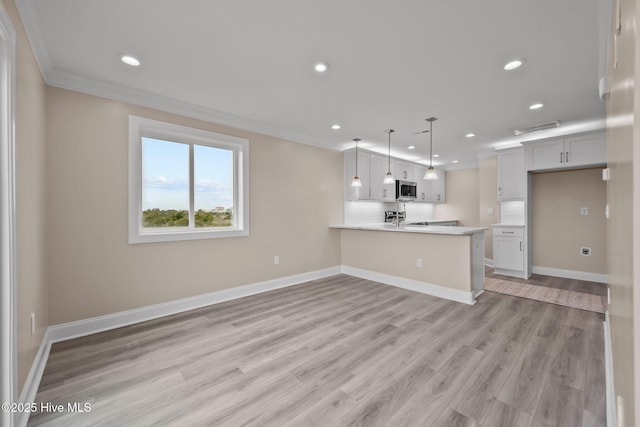 kitchen with kitchen peninsula, ornamental molding, light hardwood / wood-style floors, white cabinetry, and hanging light fixtures