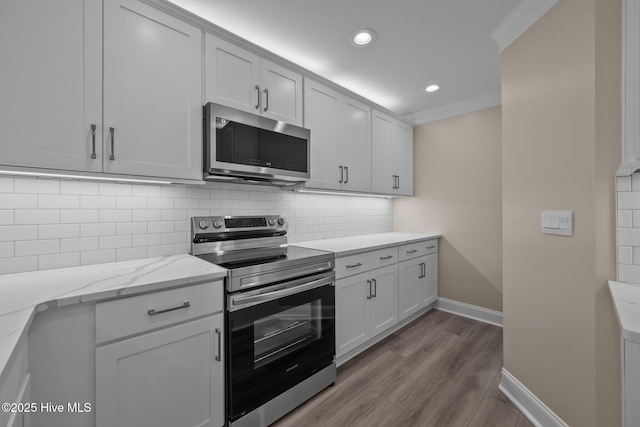 kitchen with light stone countertops, appliances with stainless steel finishes, backsplash, ornamental molding, and white cabinetry