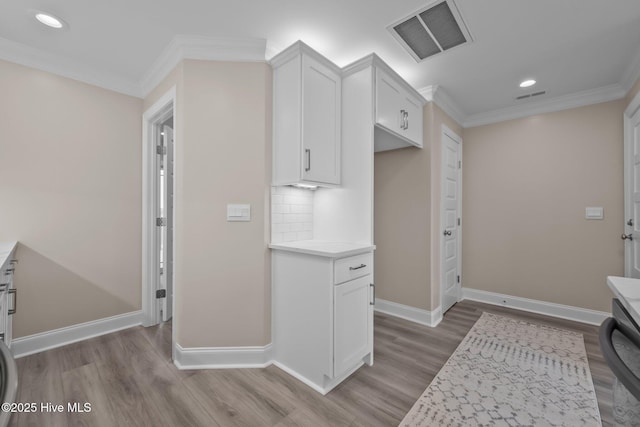 kitchen featuring tasteful backsplash, white cabinetry, light hardwood / wood-style floors, and ornamental molding