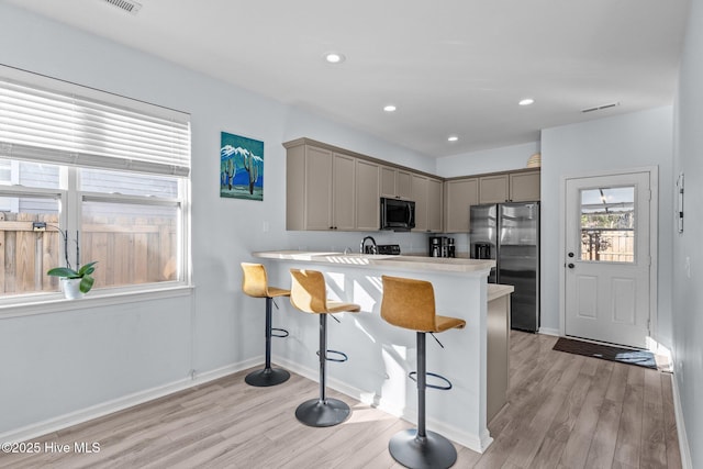 kitchen featuring kitchen peninsula, light hardwood / wood-style flooring, stainless steel fridge with ice dispenser, gray cabinetry, and a breakfast bar area