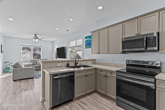 kitchen with sink, light wood-type flooring, kitchen peninsula, and appliances with stainless steel finishes