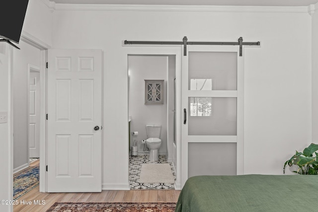 bedroom featuring crown molding, ensuite bath, a barn door, and hardwood / wood-style flooring