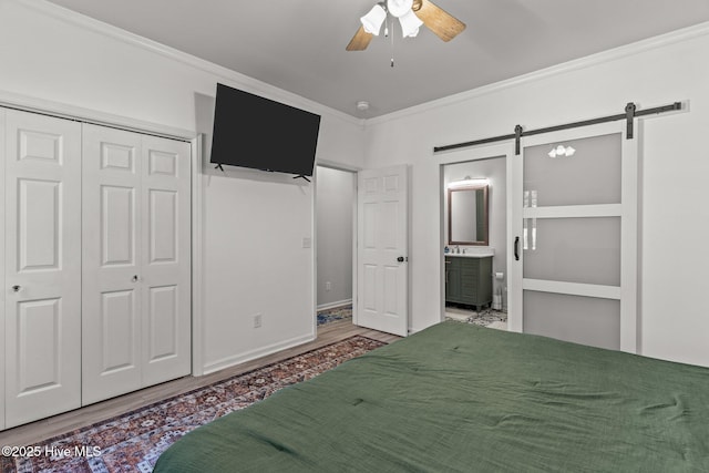 unfurnished bedroom with a closet, hardwood / wood-style floors, a barn door, crown molding, and ceiling fan