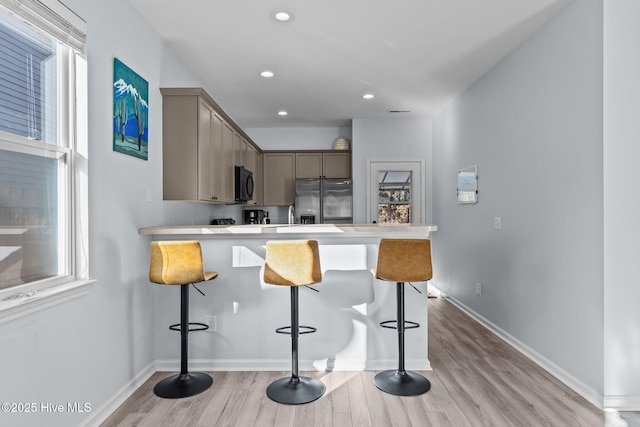 kitchen featuring kitchen peninsula, light wood-type flooring, stainless steel fridge, and a breakfast bar area