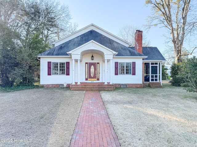 view of front of home with a shingled roof, crawl space, a chimney, and a sunroom