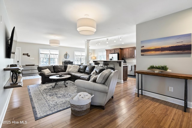 living area featuring decorative columns, baseboards, and wood finished floors