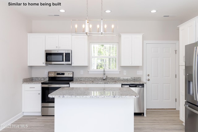 kitchen featuring decorative light fixtures, light stone counters, stainless steel appliances, and a center island