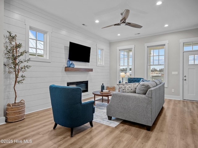 living room featuring ceiling fan, a fireplace, wood walls, and light wood-type flooring