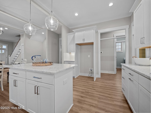 kitchen featuring a center island, hanging light fixtures, light hardwood / wood-style flooring, light stone countertops, and white cabinetry