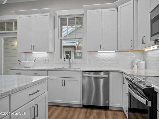 kitchen featuring sink, tasteful backsplash, appliances with stainless steel finishes, white cabinets, and hardwood / wood-style flooring