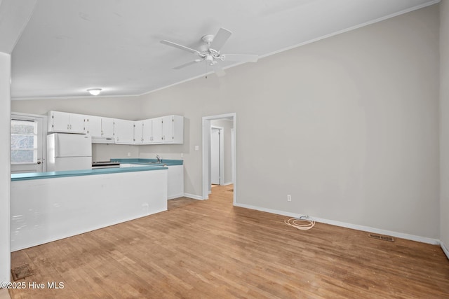 kitchen with under cabinet range hood, white cabinetry, vaulted ceiling, light countertops, and freestanding refrigerator