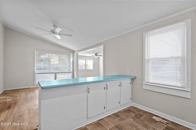 kitchen featuring baseboards, visible vents, white cabinets, lofted ceiling, and ornamental molding