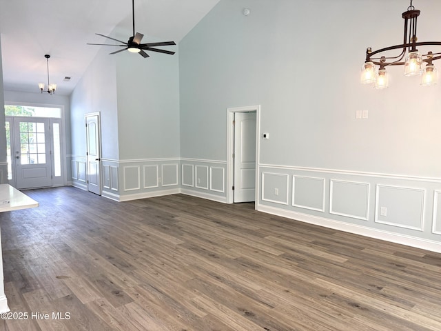 657 Boundary Loop NW, Carolina Shores, NC 28467 - unfurnished living room featuring a chandelier, high vaulted ceiling, a decorative wall, dark wood-style floors, and wainscoting