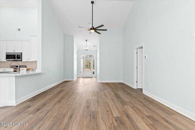 657 Boundary Loop NW, Carolina Shores, NC 28467 - unfurnished living room with high vaulted ceiling, ceiling fan, wood finished floors, and baseboards