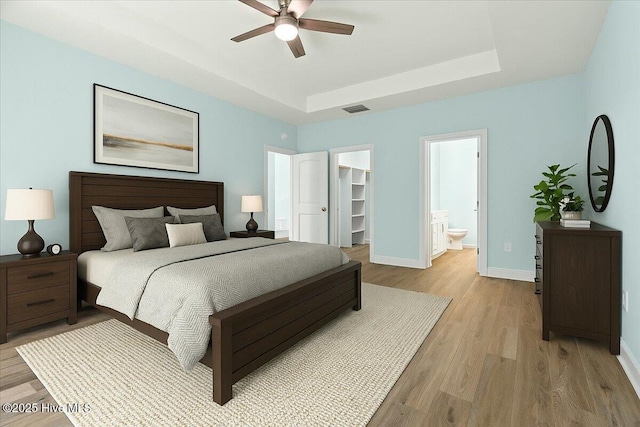 657 Boundary Loop NW, Carolina Shores, NC 28467 - bedroom featuring a raised ceiling, a walk in closet, light wood-type flooring, baseboards, and ensuite bath