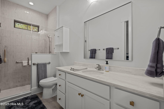 bathroom with toilet, vanity, a tile shower, and hardwood / wood-style flooring