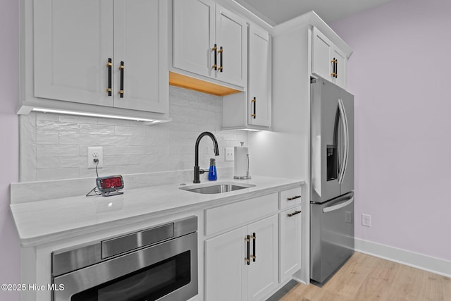 kitchen featuring appliances with stainless steel finishes, tasteful backsplash, light wood-type flooring, white cabinets, and sink