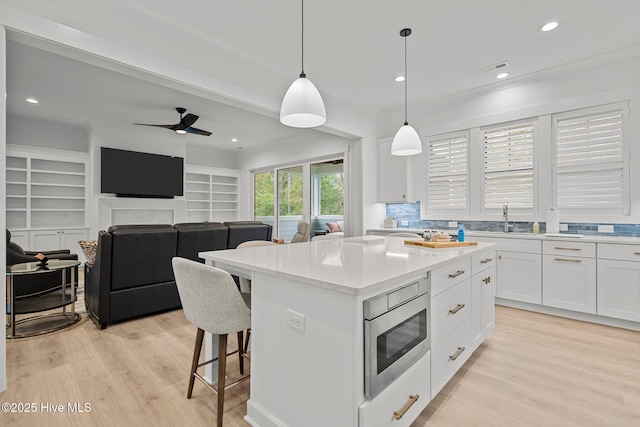 kitchen featuring stainless steel microwave, decorative light fixtures, built in features, white cabinets, and a center island