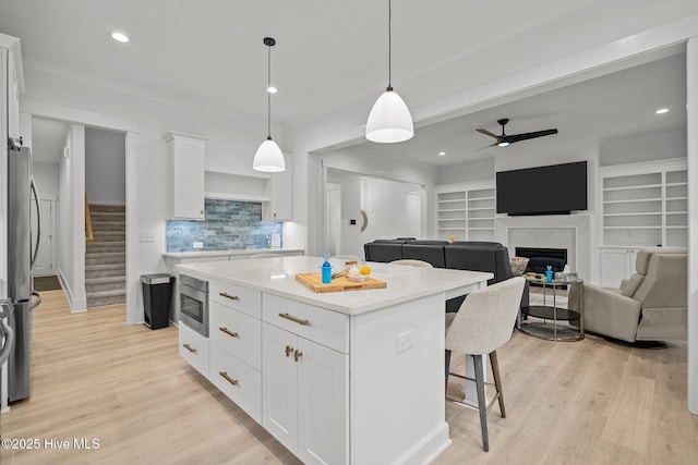 kitchen with decorative light fixtures, a fireplace, a center island, stainless steel appliances, and white cabinets