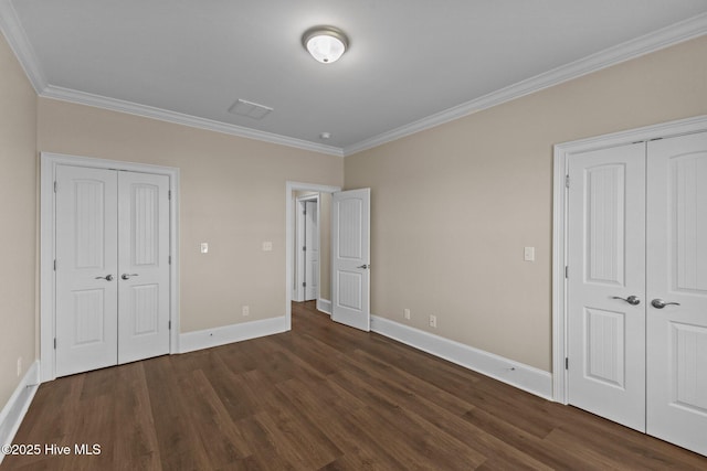 unfurnished bedroom with dark hardwood / wood-style flooring, crown molding, and two closets