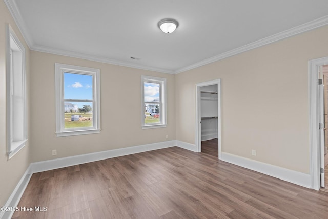 unfurnished bedroom featuring a closet, a walk in closet, ornamental molding, and hardwood / wood-style flooring