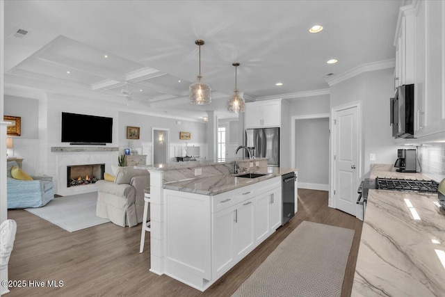 kitchen featuring white cabinets, an island with sink, decorative light fixtures, and appliances with stainless steel finishes