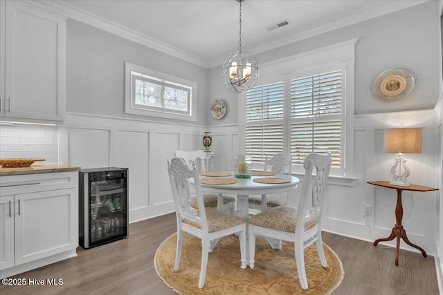 dining room featuring a notable chandelier, light wood-type flooring, ornamental molding, and beverage cooler