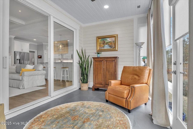 living area with ornamental molding, dark tile patterned flooring, a healthy amount of sunlight, and wood walls