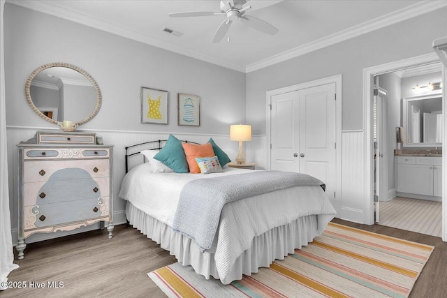 bedroom featuring ceiling fan, crown molding, ensuite bathroom, a closet, and hardwood / wood-style flooring