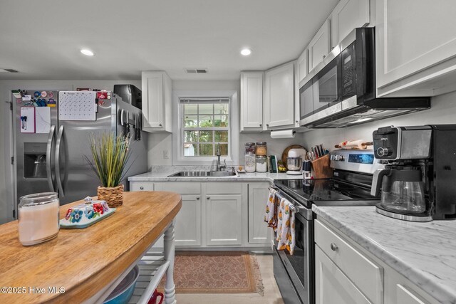 kitchen featuring light stone countertops, light wood-type flooring, white cabinetry, and stainless steel appliances