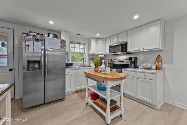 kitchen with a kitchen breakfast bar, white cabinets, light hardwood / wood-style floors, and appliances with stainless steel finishes