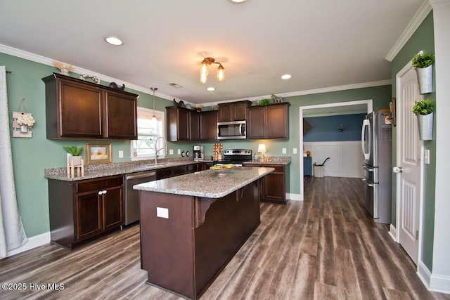 kitchen featuring ornamental molding, appliances with stainless steel finishes, decorative light fixtures, a kitchen island, and dark brown cabinetry