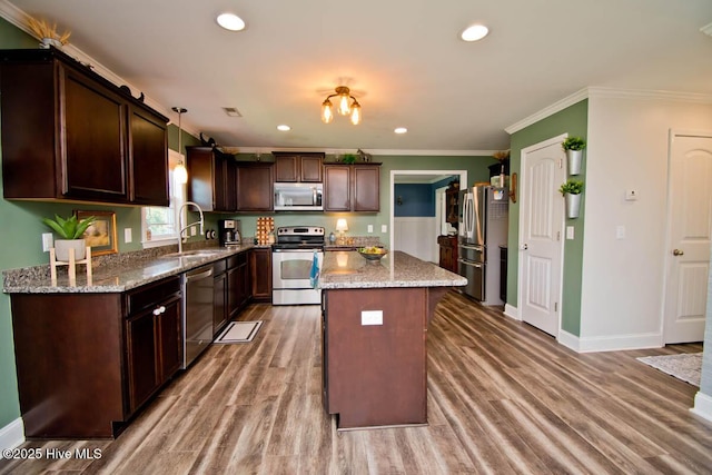 kitchen with light stone countertops, stainless steel appliances, sink, pendant lighting, and a kitchen island