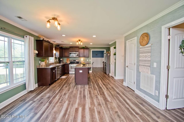 kitchen featuring dark brown cabinetry, stainless steel appliances, crown molding, sink, and a center island