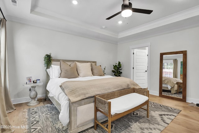 bedroom featuring hardwood / wood-style flooring, ornamental molding, a raised ceiling, and ceiling fan