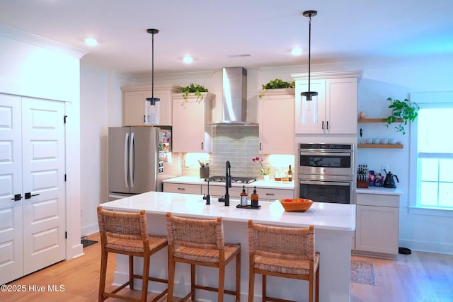 kitchen featuring decorative light fixtures, decorative backsplash, appliances with stainless steel finishes, an island with sink, and wall chimney exhaust hood