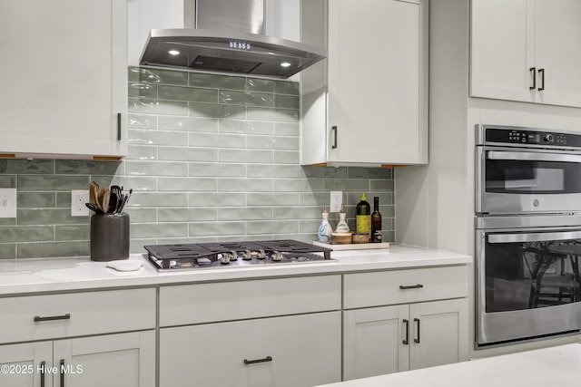 kitchen with backsplash, stainless steel appliances, light stone counters, island range hood, and white cabinets