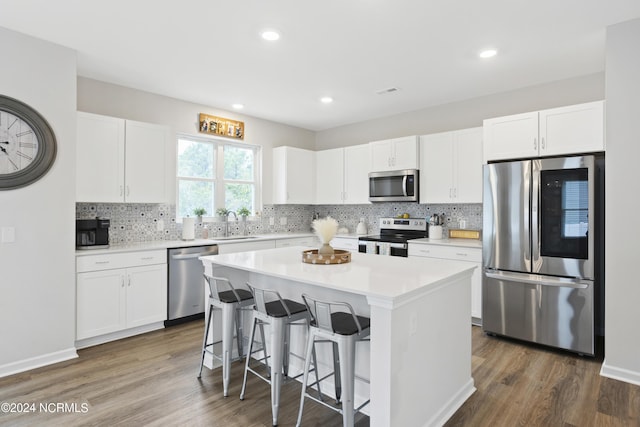 kitchen with stainless steel appliances, a kitchen island, dark hardwood / wood-style floors, a kitchen bar, and white cabinets