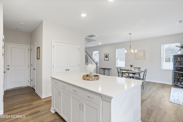 kitchen with hardwood / wood-style floors, plenty of natural light, decorative light fixtures, a kitchen island, and white cabinetry