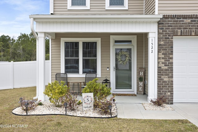 entrance to property featuring a porch, a yard, and a garage