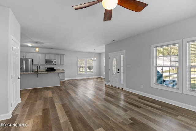 unfurnished living room featuring ceiling fan with notable chandelier, dark hardwood / wood-style flooring, and sink