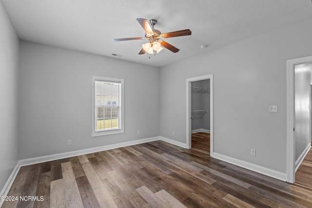 unfurnished bedroom with a spacious closet, ceiling fan, dark wood-type flooring, a textured ceiling, and a closet