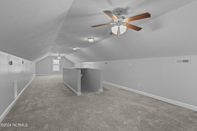 additional living space with a textured ceiling, light colored carpet, vaulted ceiling, and ceiling fan